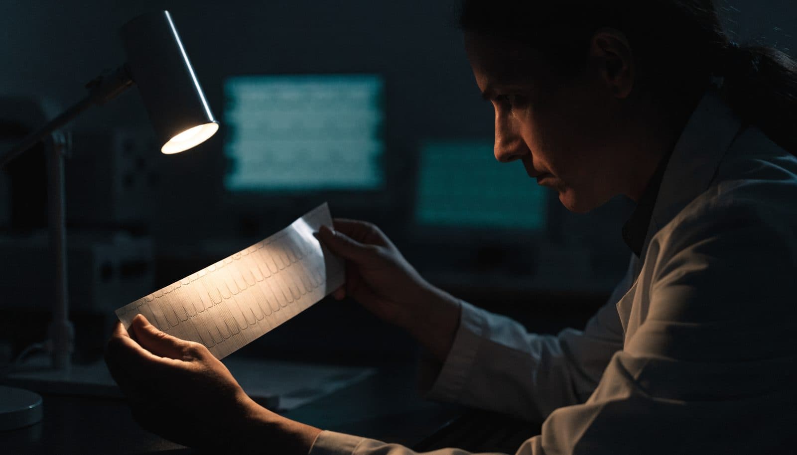 A cardiologist reading a printed ECG rhythm strip under a desk lamp