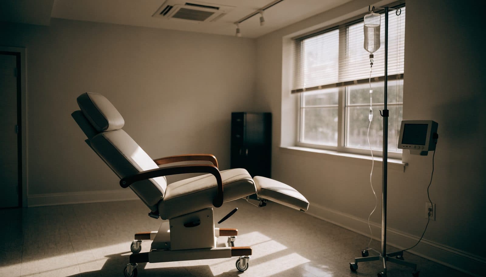 An empty infusion chair beside a window in an oncology treatment room