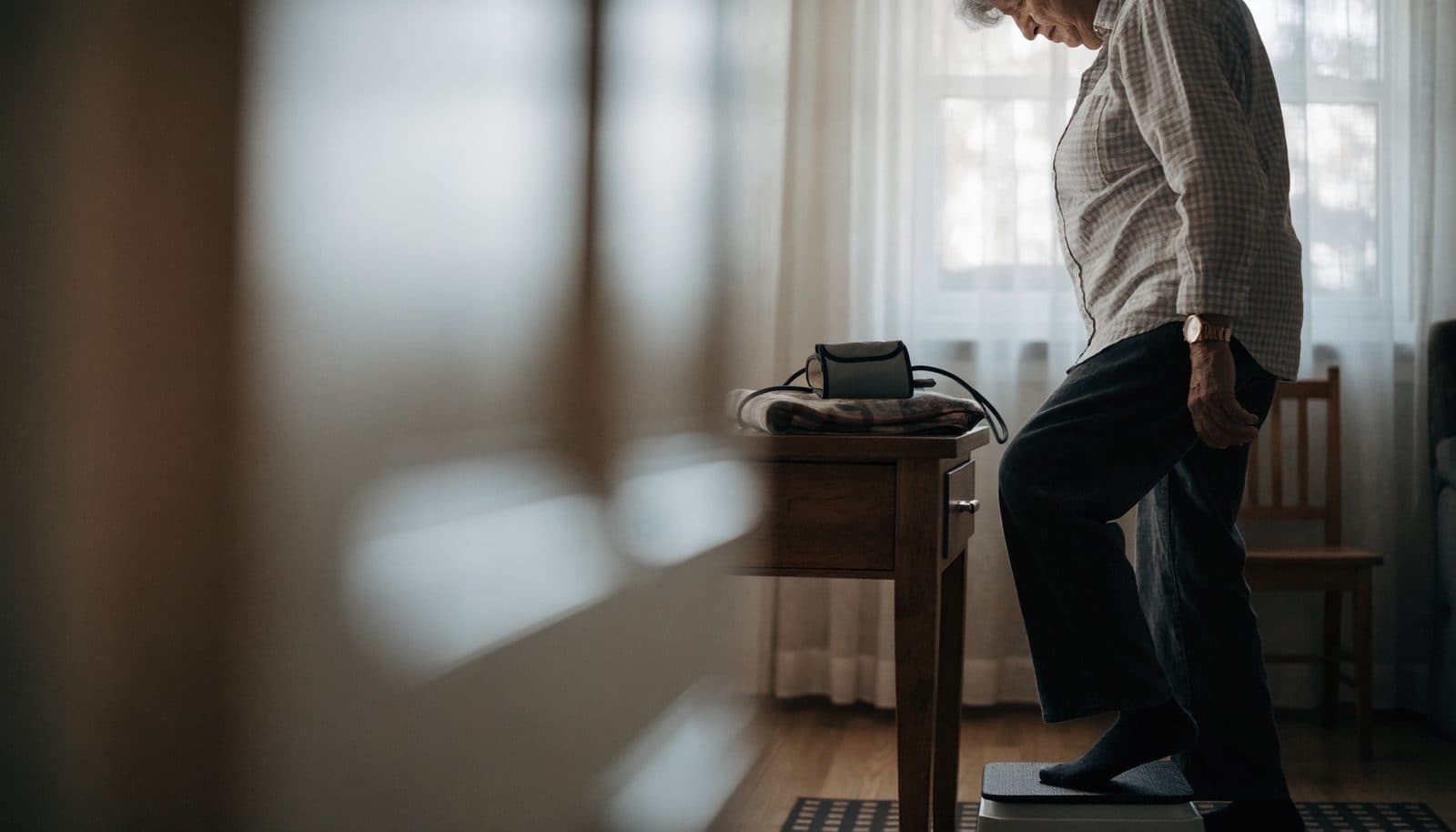 An older adult weighing themselves at home beside a blood pressure cuff