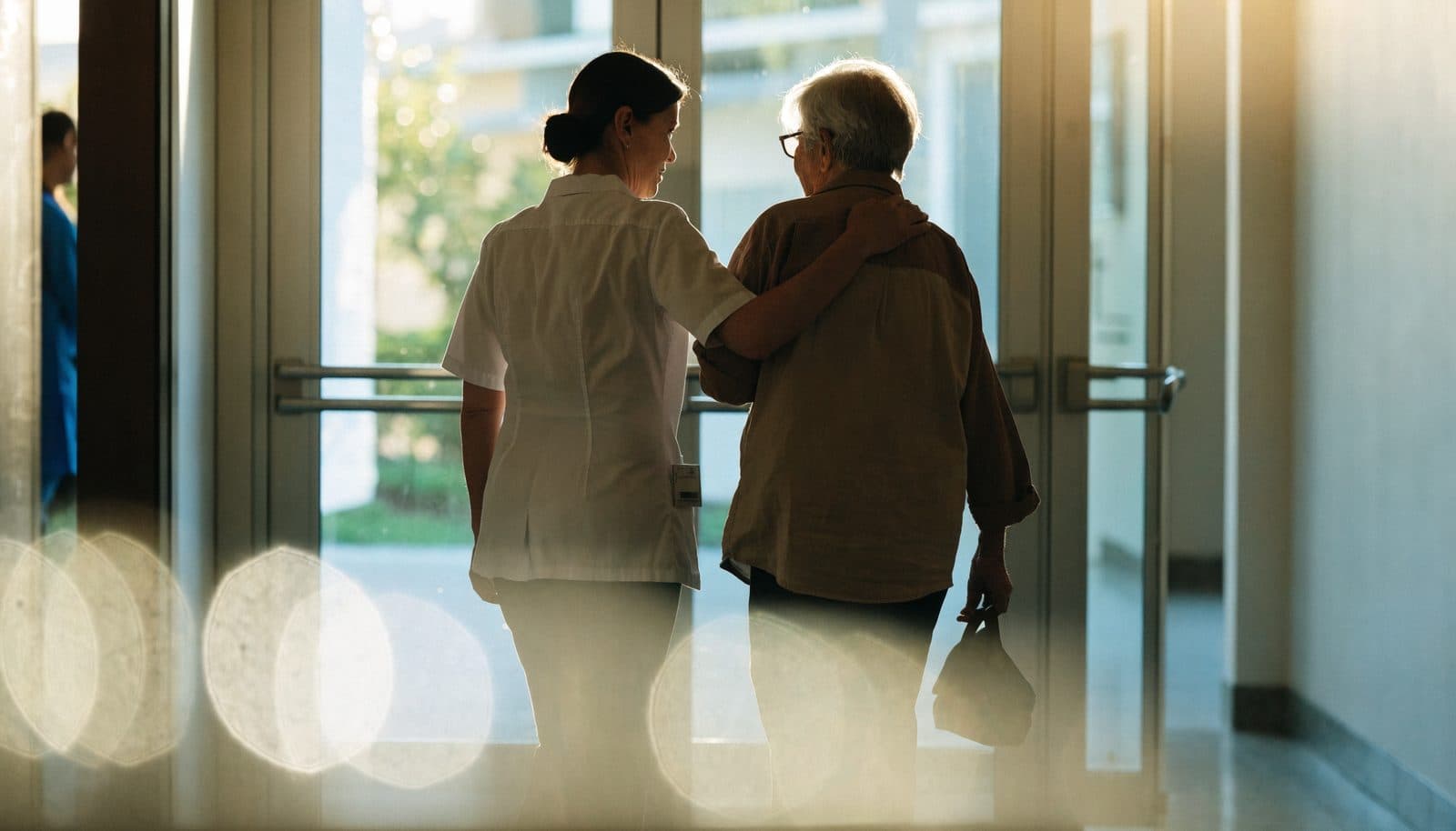A nurse walking an older patient out through hospital doors on discharge day